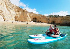 A couple on SUPs in front of a beautiful beach during the SUP Tour to the Benagil Cave from Blue Xperiences Algarve.