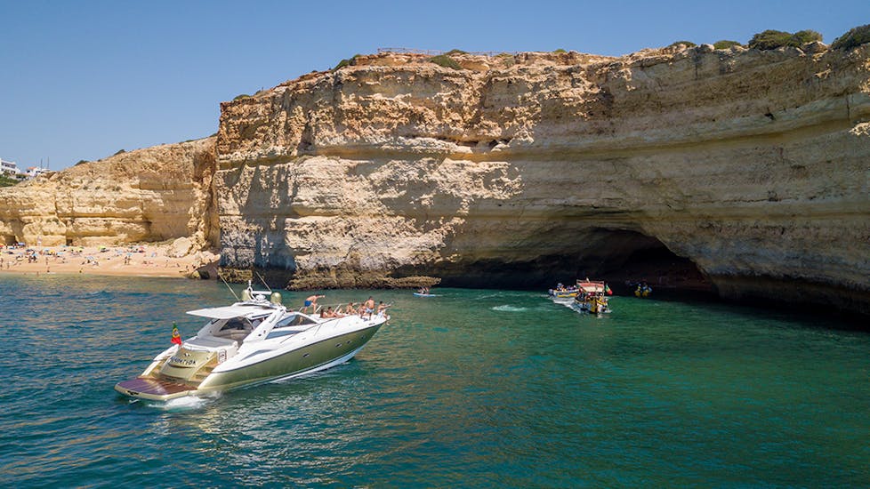 A boat anchors next to a beach while doing a Private Boat Trip to Benagil Cave & Alfanzina Lighthouse with Snorkeling organized by EasyDream Charters Albufeira.