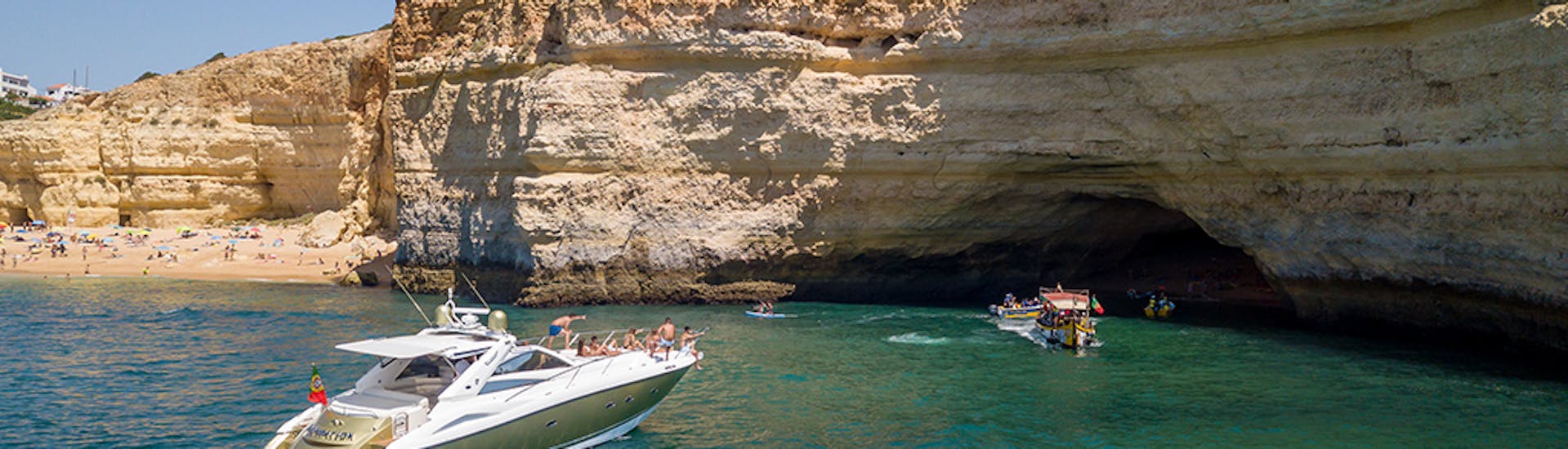 A boat anchors next to a beach while doing a Private Boat Trip to Benagil Cave & Alfanzina Lighthouse with Snorkeling organized by EasyDream Charters Albufeira.