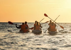 Menschen paddeln in ihren Kajaks dem Sonnenuntergang entgegen, während ihrer Sonnenuntergangs Kayaktour in Piran mit Sea Kayak Piran.
