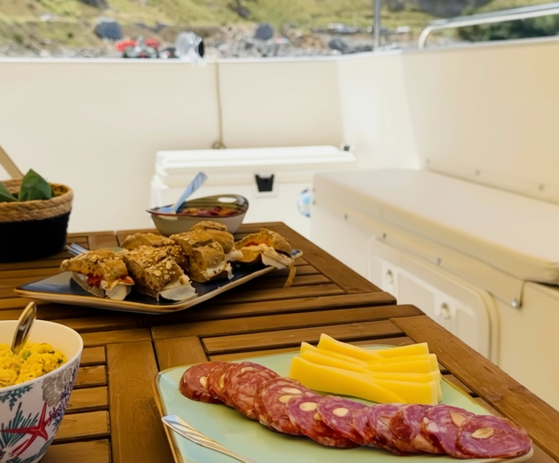 Aperitivo con bocadillos y salami en un paseo en barco. Durante una excursión en barco desde Mondello a la Reserva de Capo Gallo con Boat Tour Mondello, se sirve un delicioso aperitivo de sándwiches, salami y queso en una mesa de madera.