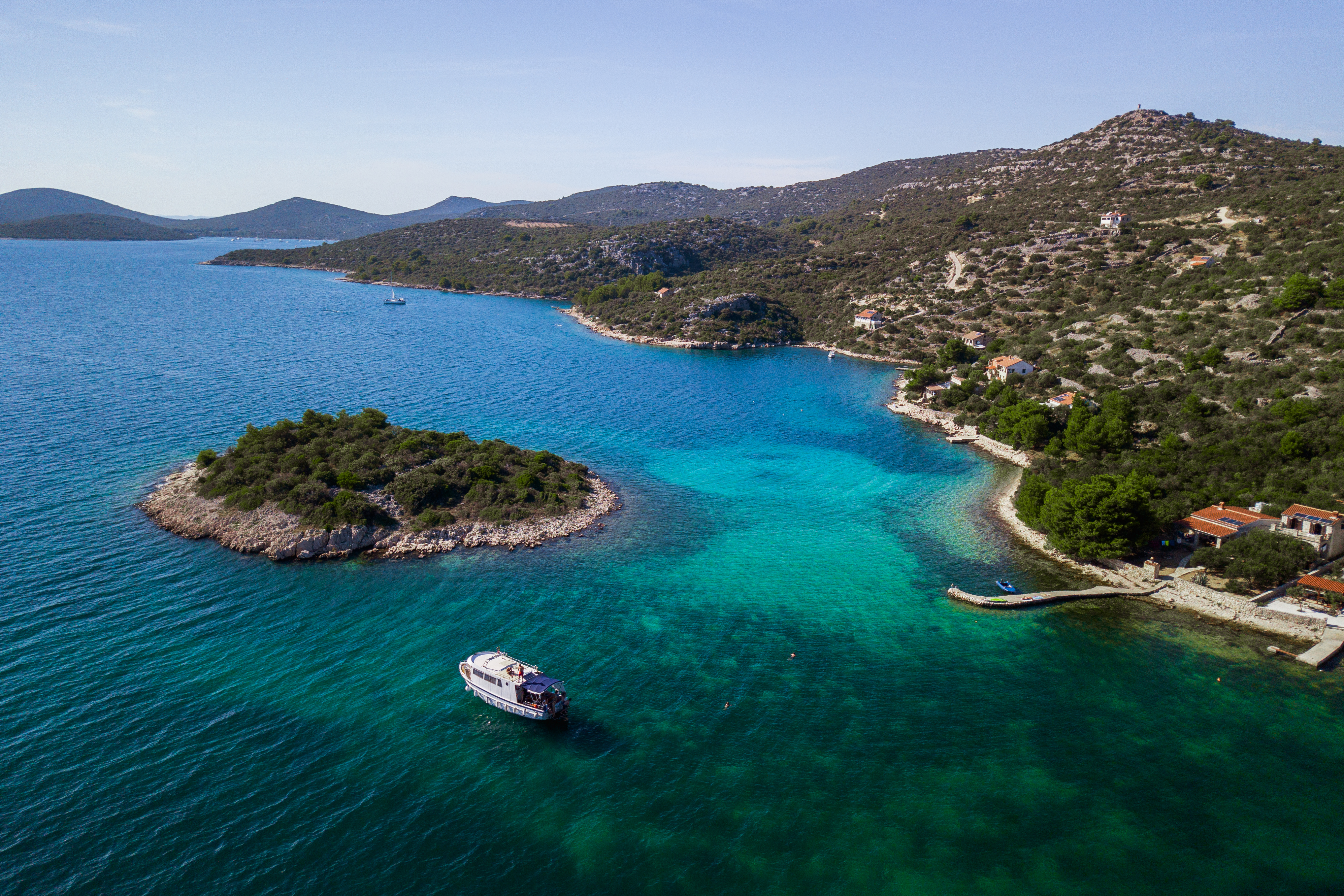 The Škver Tours Biograd na Moru boat sails through a turquoise bay past a small, green island during a boat trip to the National Park Kornati with lunch.