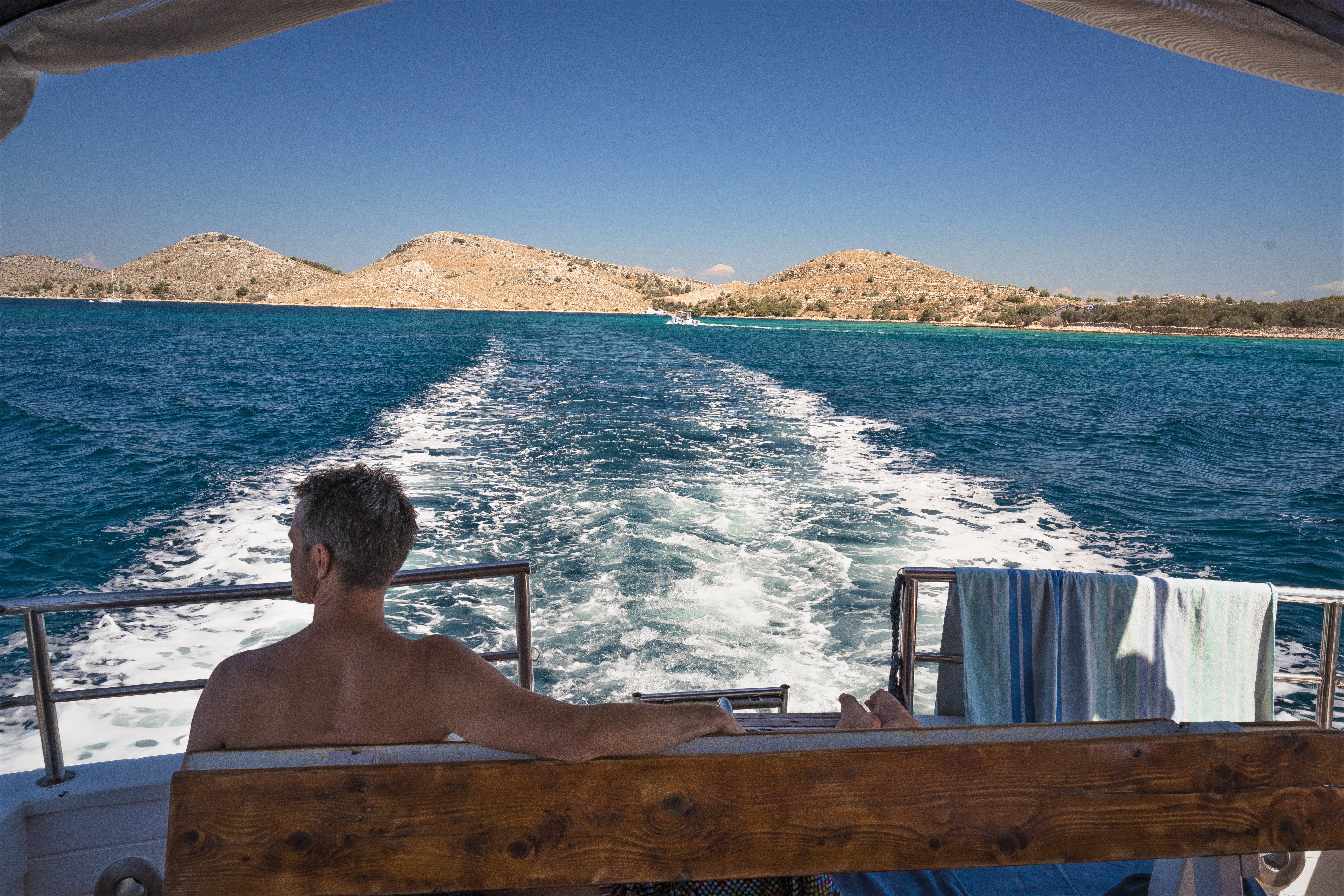 A man enjoys the view from the back of a boat during a boat trip to the National Park Kornati with lunch by Škver Tours Biograd na Moru.
