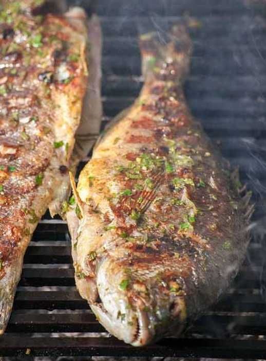 Two whole fish seasoned with herbs are sizzling on a grill, part of the all-inclusive meal on the 'Discover Island Plavnik with a Pirate Ship' tour by M/B Kosljun Punat.