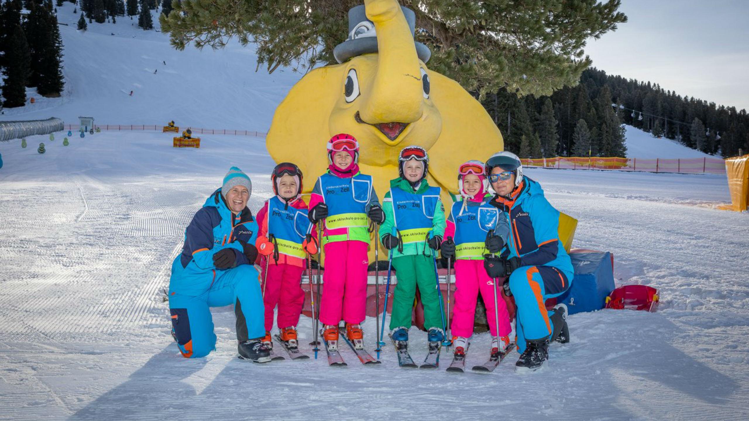 A group of children and their two ski instructors from the ski school Skischule Pro Zell in Zell am Ziller are posing for a photo in the Kinderland area during their Kids Ski Lessons (from 6 years) - Advanced .