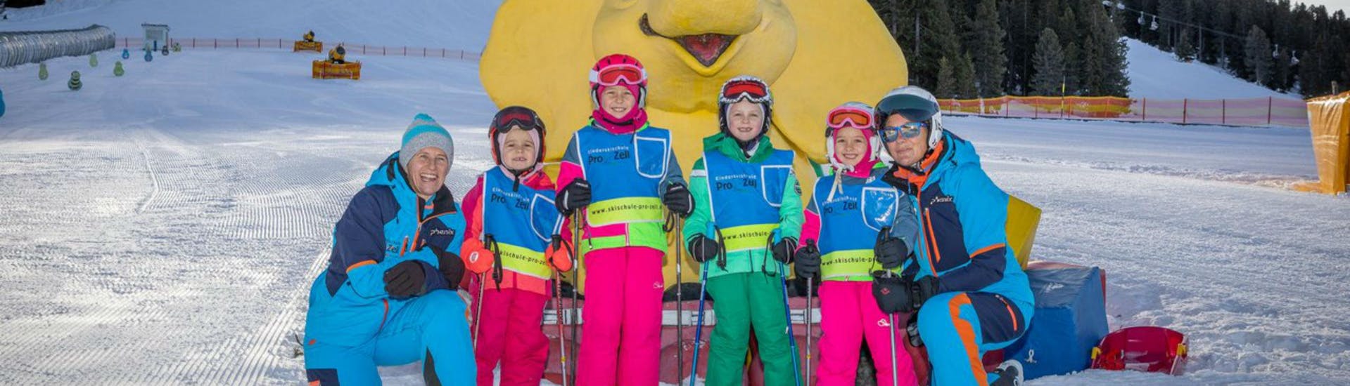 A group of children and their two ski instructors from the ski school Skischule Pro Zell in Zell am Ziller are posing for a photo in the Kinderland area during their Kids Ski Lessons "Bambini" (3-5 years).