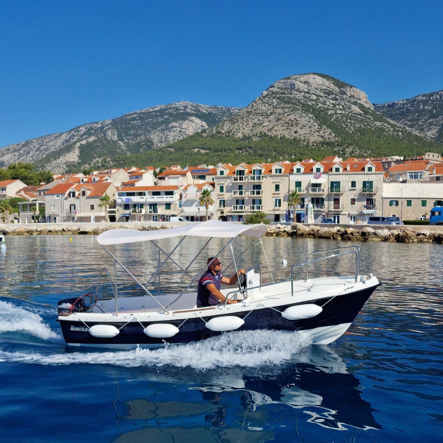 Imagen de un barco navegando por aguas azules, frente a la ciudad durante un alquiler de barco sin licencia en Bol con Maestral Travel Bol.