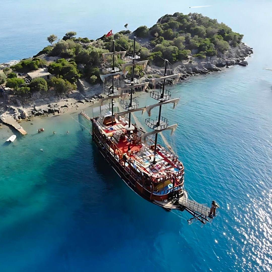 Imagen aérea de un barco pirata anclado en aguas cristalinas junto a una isla durante un paseo en barco pirata desde Ölüdeniz con natación, almuerzo y fiesta de espuma de Black Pearl Tours Ölüdeniz.