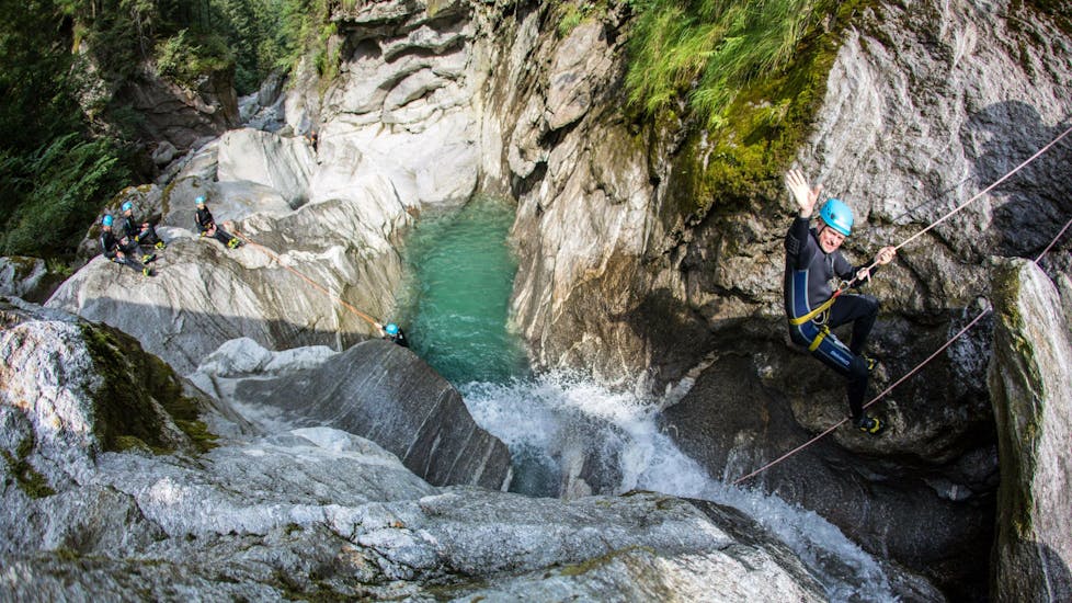 Ein Teilnehmer der Tour Canyoning “Blue Lagoon” für Mutige - Zemmschlucht von Mountain Sports Mayrhofen winkt in die Kamera während er sich in die Schlucht hinabseilt.