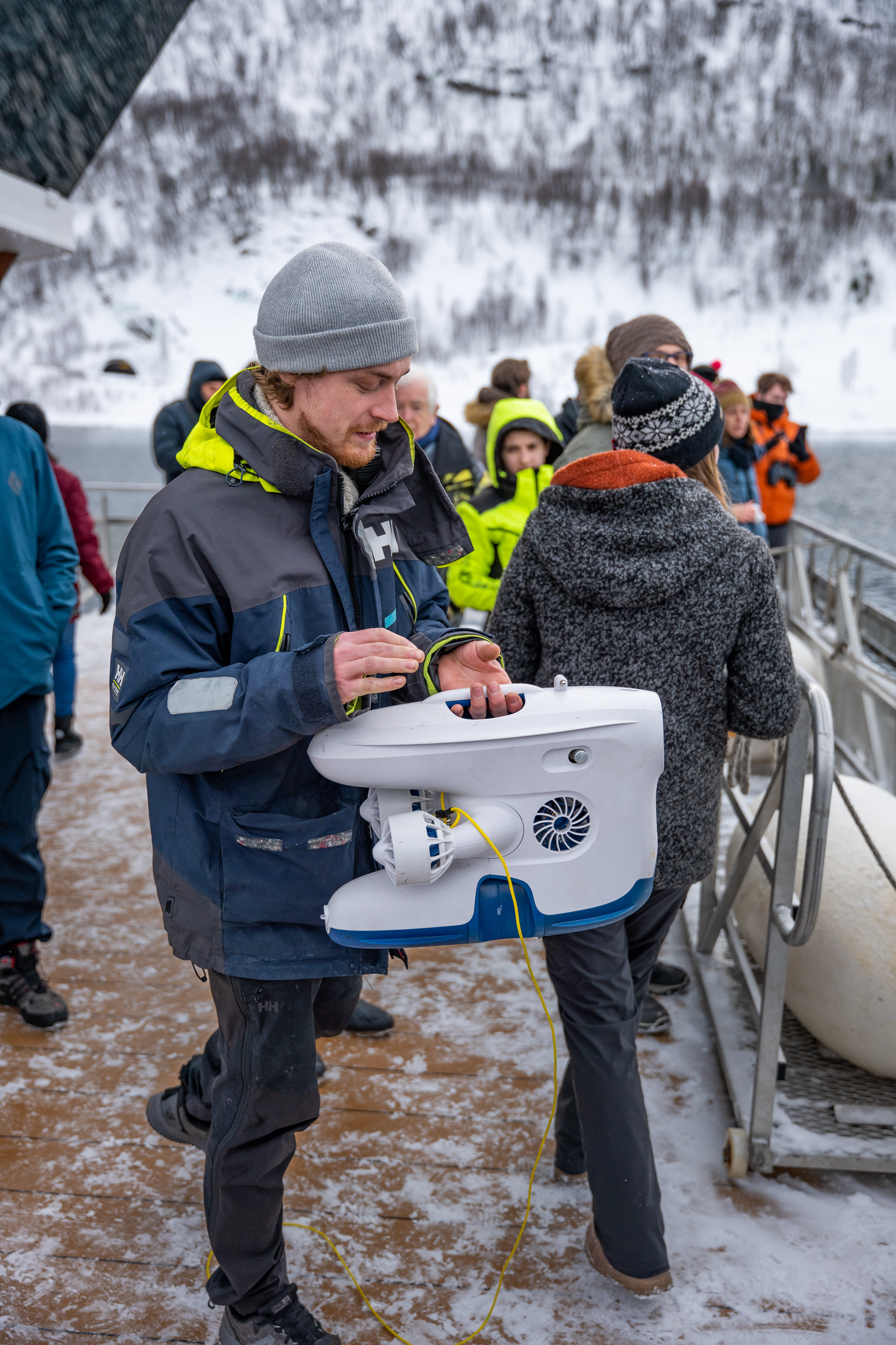 Un guía sostiene un dron submarino en la cubierta nevada de un catamarán durante una excursión en barco desde Tromsø a través del fiordo de Ramfjord, con una experiencia de avistamiento de fauna y naturaleza a cargo de Brim Explorer Norway.
