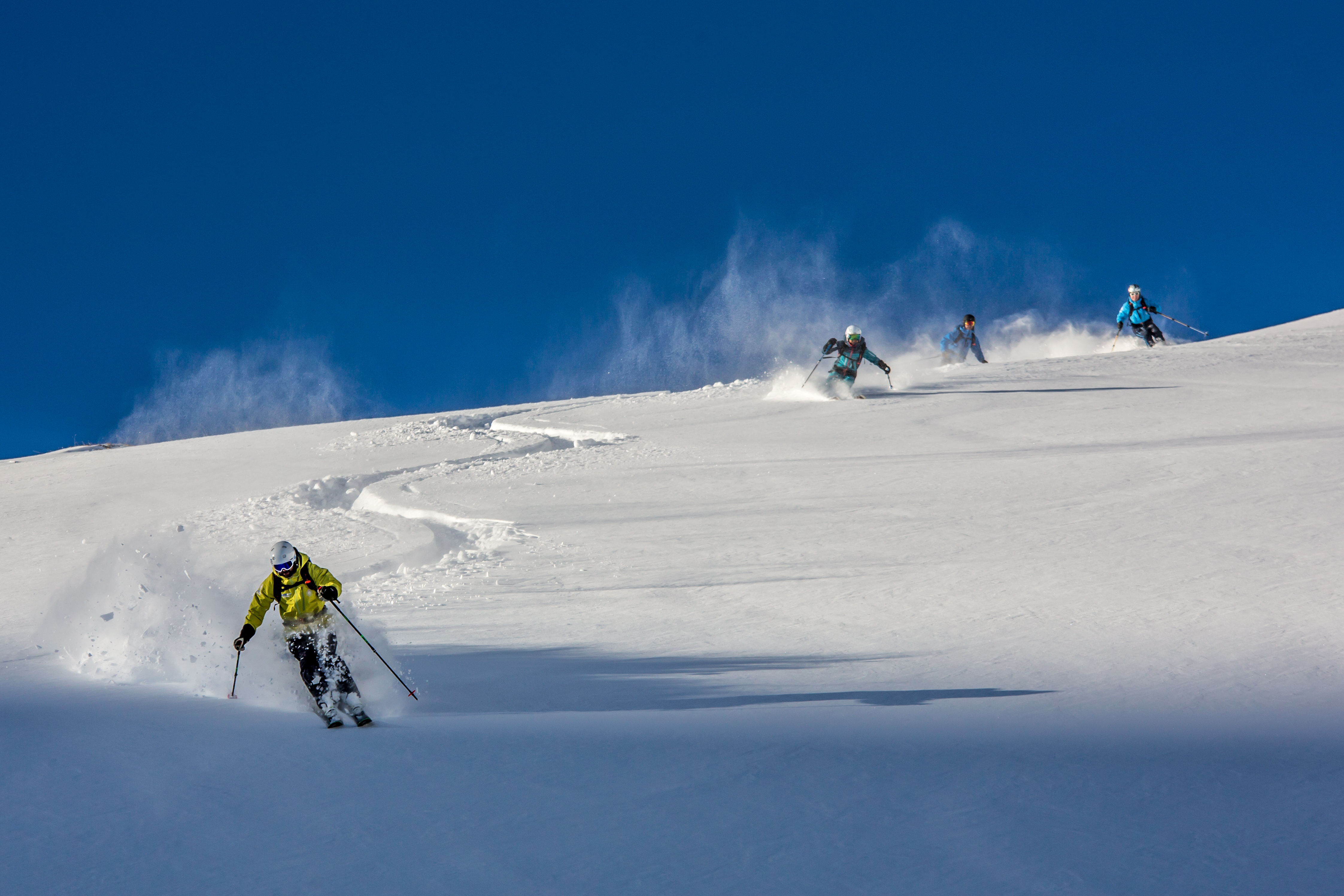 Mehrere Skifahren fahren währen ihrem Freeriden Intermediates Kurs abseits der Pisten. 