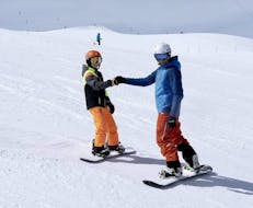 Un moniteur de snowboard s'amuse sur une pente avec un jeune snowboarder lors d'un cours privé de snowboard pour enfants organisée par l'école de ski Ski- und Snowboardschule SNOWLINES à Sölden. 
