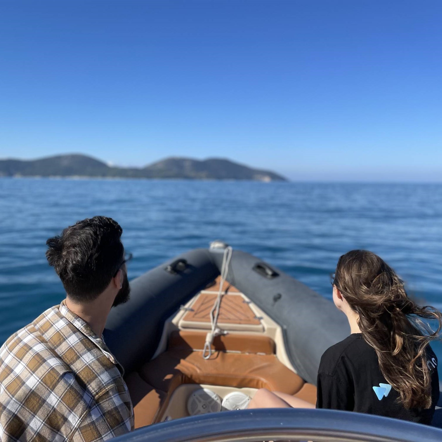 Beeld van twee mensen op een boot die richting verre heuvels varen over kalm blauw water, tijdens een boottocht van Vlorë naar het eiland Sazan, de Haxhi Ali-grot en Karaburun met zwemmen van TripMe Today Vlore.