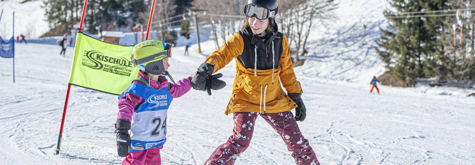 An older child helping a younger one during their kids ski lessons for beginners with skischule Bad Hofgastein.