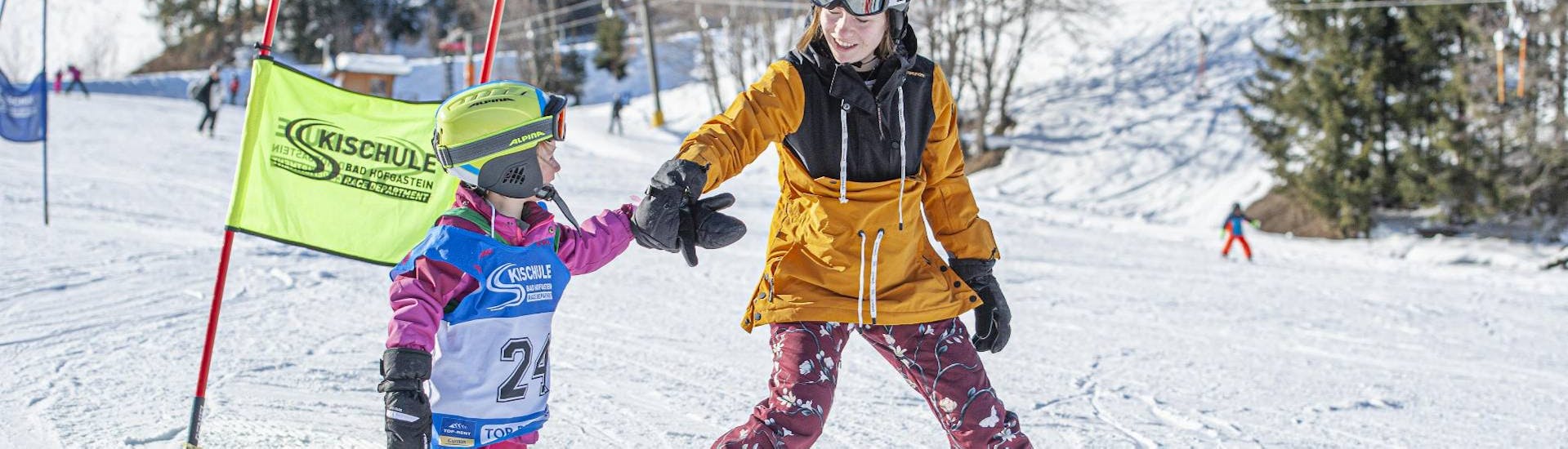 Ein älteres Kind hilft einem jüngeren Kind beim Kinder-Skikurs für Anfänger in der Skischule Bad Hofgastein.