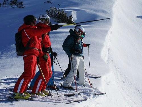 Clases de esquí para adultos de nivel avanzado con S4 Snowsport Fieberbrunn El instructor de esquí utiliza el bastón de esquí para mostrar a los participantes dónde continúa el curso durante las clases de esquí para adutos - nivel avanzado de la escuela de esquí S4 Snowsports Fieberbrunn.