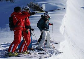 The ski instructor uses the ski pole to show the participants where the course continues during the ski lessons for adults - advanced of the ski school S4 Snowsports Fieberbrunn.