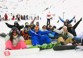 A group of snowboarders is sitting in the snow surrounding their snowboard instructor from the ski school Prosneige Méribel during their Snowboarding Lessons for Adults - All Levels.