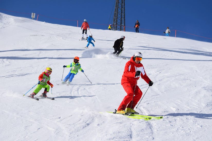 Eine Gruppe von Kindern folgt ihrem Skilehrer die Pisten hinunter, während des privaten Kinder-Skikurses für alle Altersgruppen mit der Skischule Snowsports Westendorf.