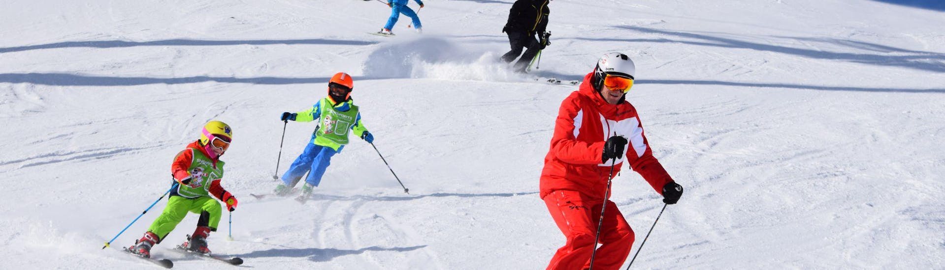 Eine Gruppe von Kindern folgt ihrem Skilehrer die Pisten hinunter, während des privaten Kinder-Skikurses für alle Altersgruppen mit der Skischule Snowsports Westendorf.
