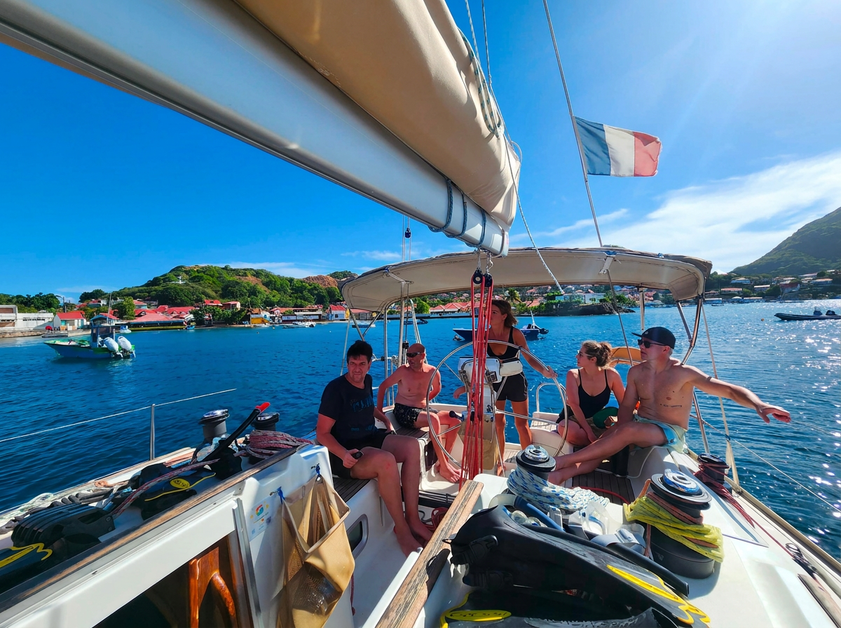 Zeiltocht naar Les Saintes met Reve de Nav' Croisière Een groep reizigers ontspant op het dek van een zeilboot die voor anker ligt in een turquoise baai tijdens een zeiltocht naar Les Saintes met Reve de Nav' Croisière.