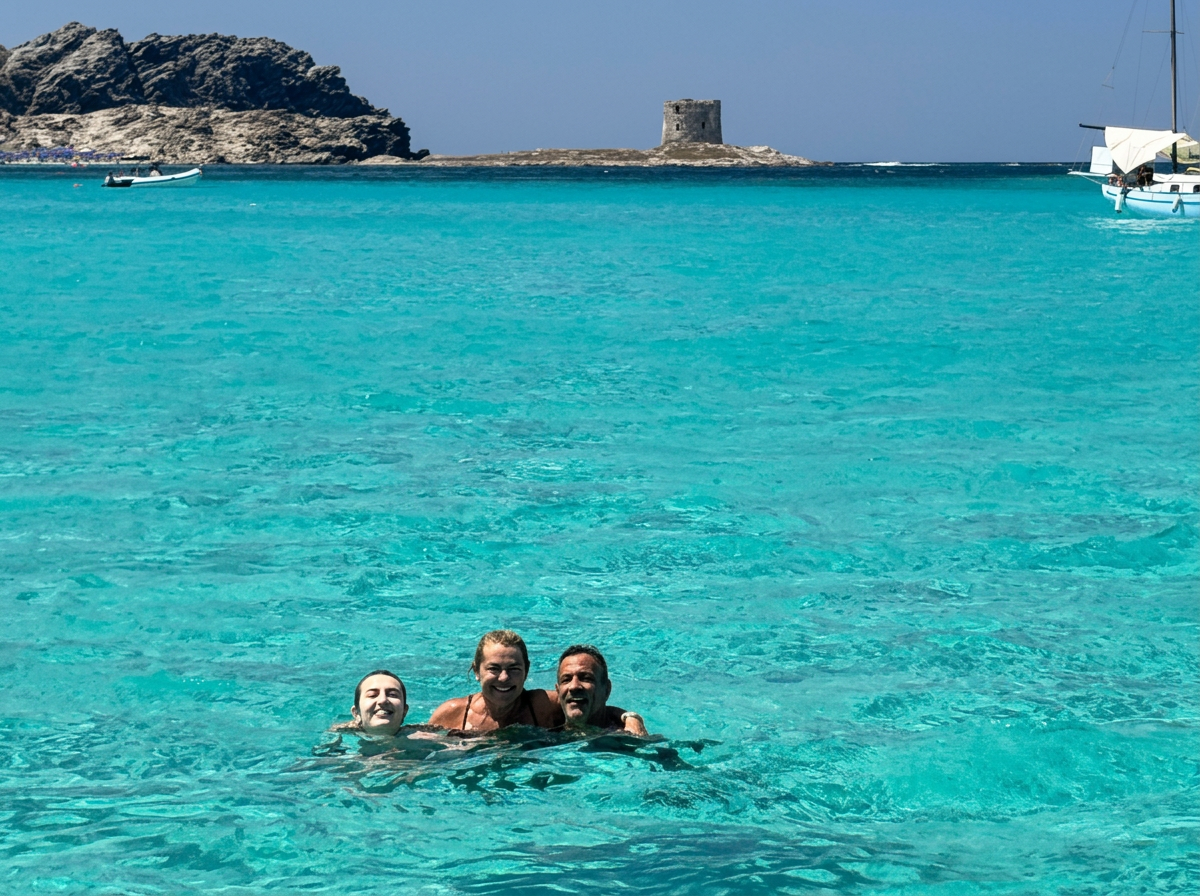 Nadar en las aguas cristalinas de La Pelosa Tres personas sonríen mientras nadan en el mar turquesa cerca de la torre La Pelosa durante una excursión privada en lancha neumática por el Parque Nacional de Asinara con Sottovento Escursioni Asinara.
