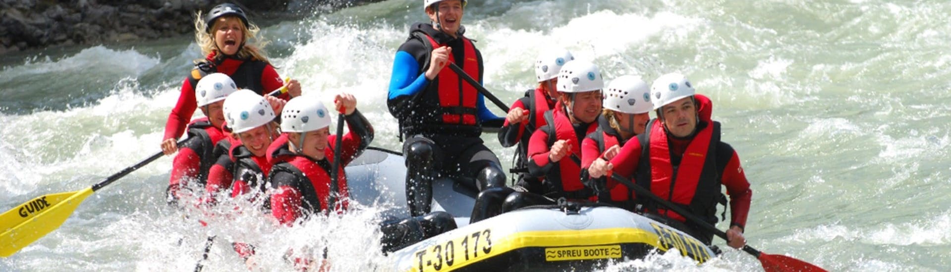 A group of people is navigating their dinghy across the tumultuous rapids of the Inn River during while Rafting in the Imster Schlucht with CanKick Ötztal.