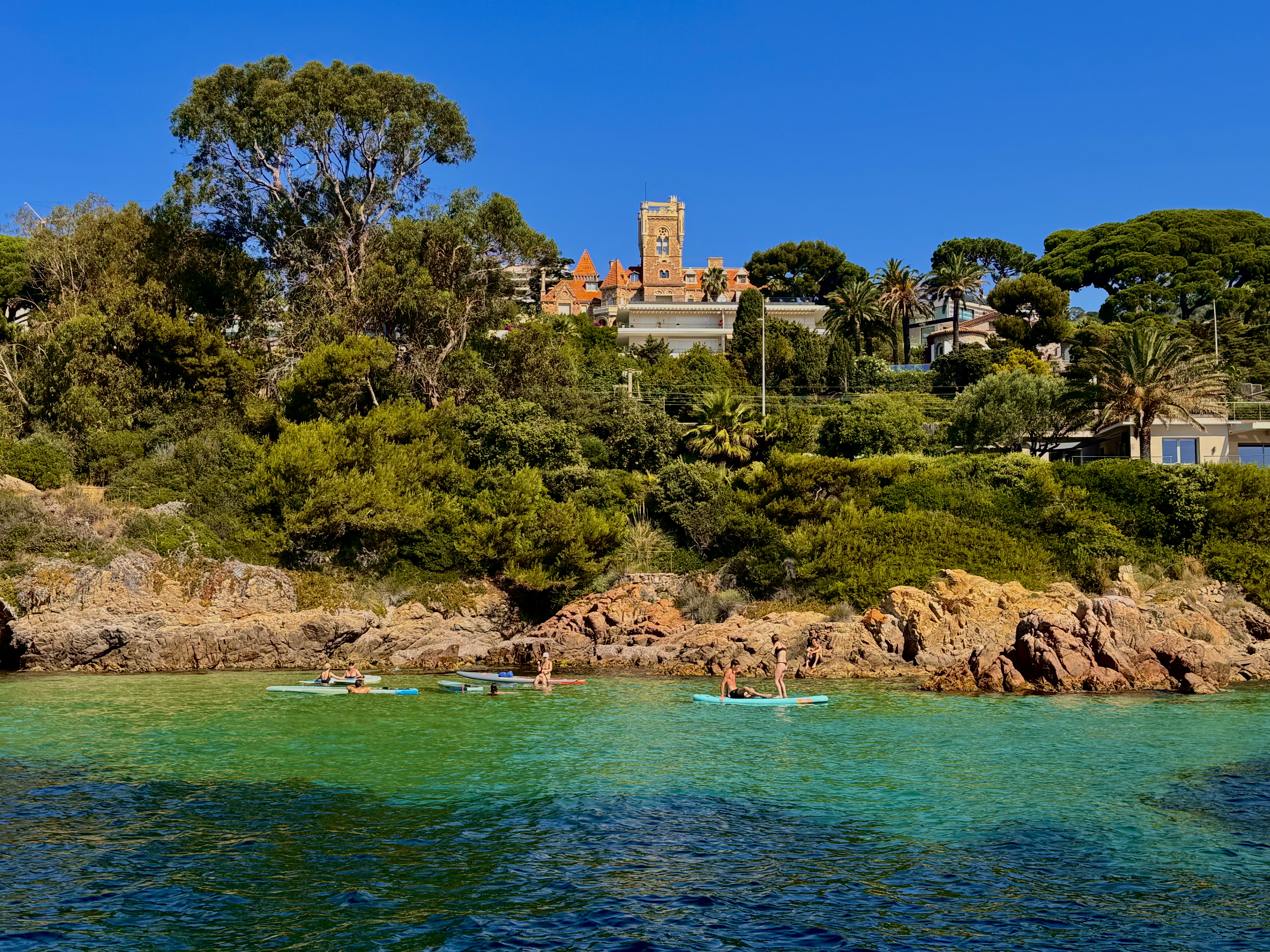 Groupe de personnes sur des planches à pagaie dans une crique turquoise à Antibes. Un groupe de personnes en paddleboard profite de l'eau claire et turquoise lors d'une pause baignade pendant leur excursion en voilier à Antibes avec Cap Sail Aventures Antibes.