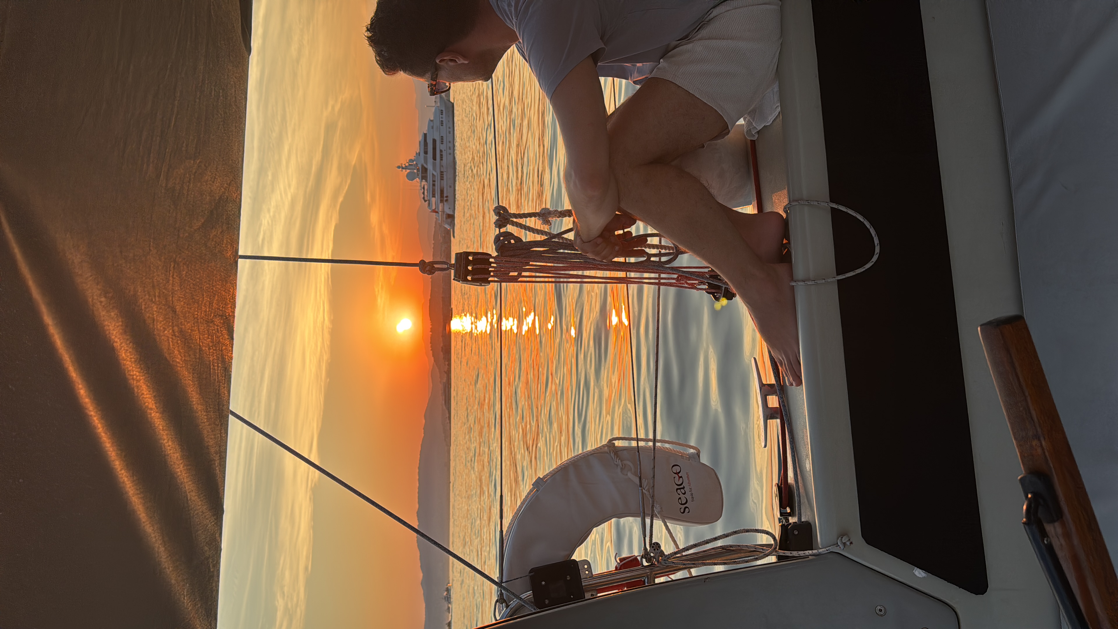 Man sailing a boat during a vibrant sunset A man adjusts the rigging on a sailboat during a sunset aperitif cruise with Cap Sail Aventures Antibes, as the sun sets over the water off the coast of Antibes.
