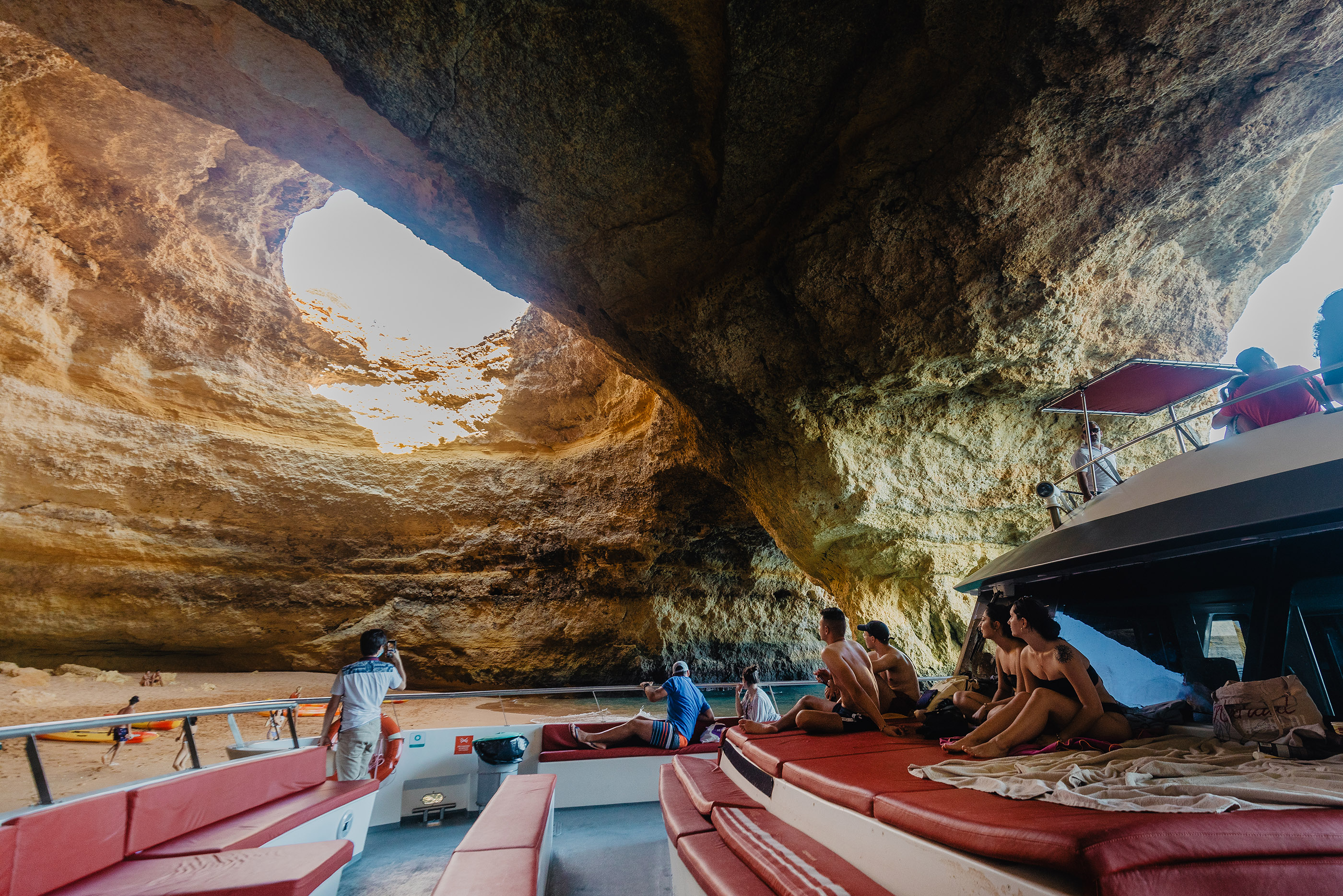 The AlgarExperience catamaran sails through the Benagil Caves near Albufeira, with passengers relaxing on the deck and admiring the view.