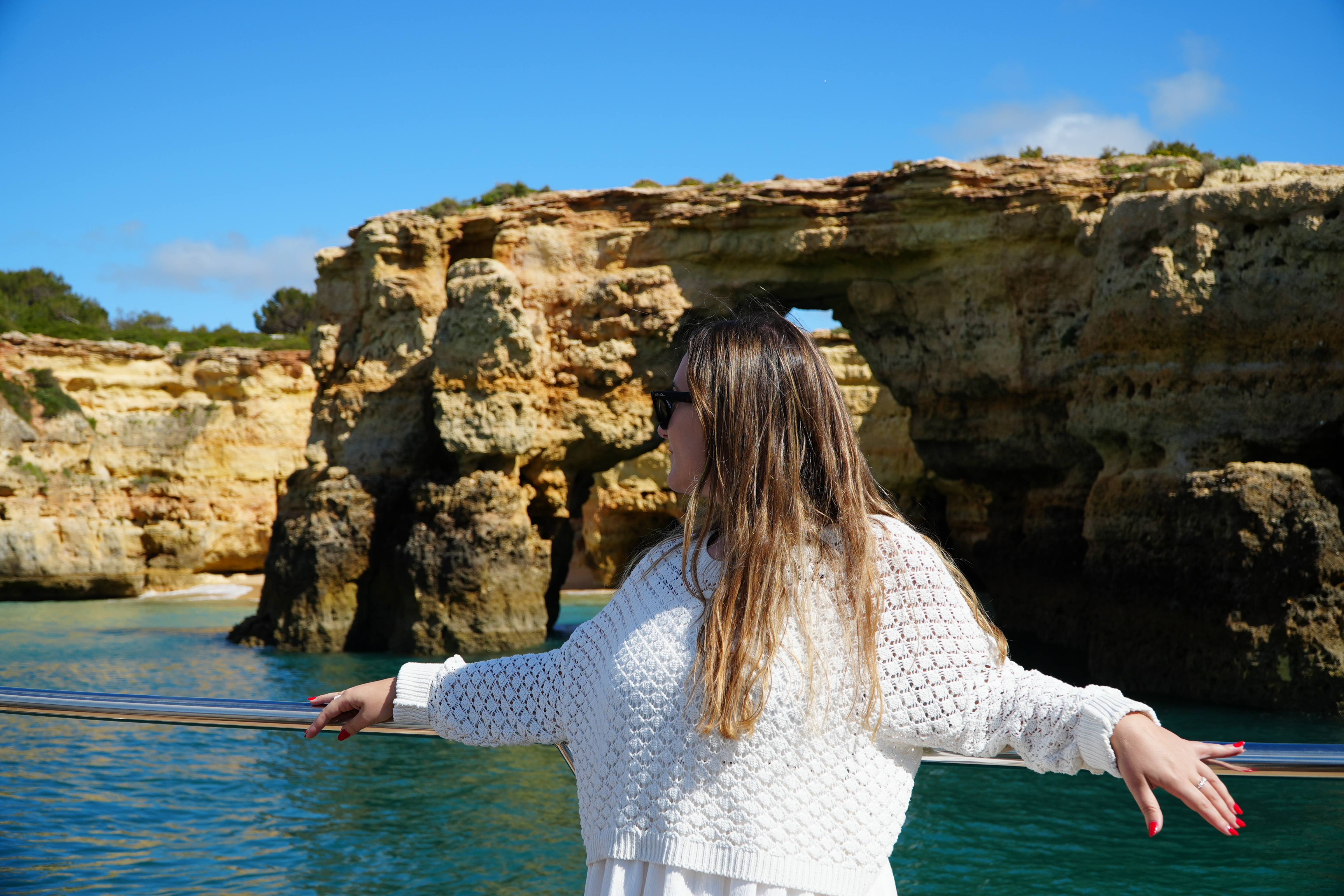 A woman on the Albufeira - Benagil Caves & Coastline Catamaran tour by AlgarExperience enjoys the view of the stunning sea arch and cliffs from the boat.