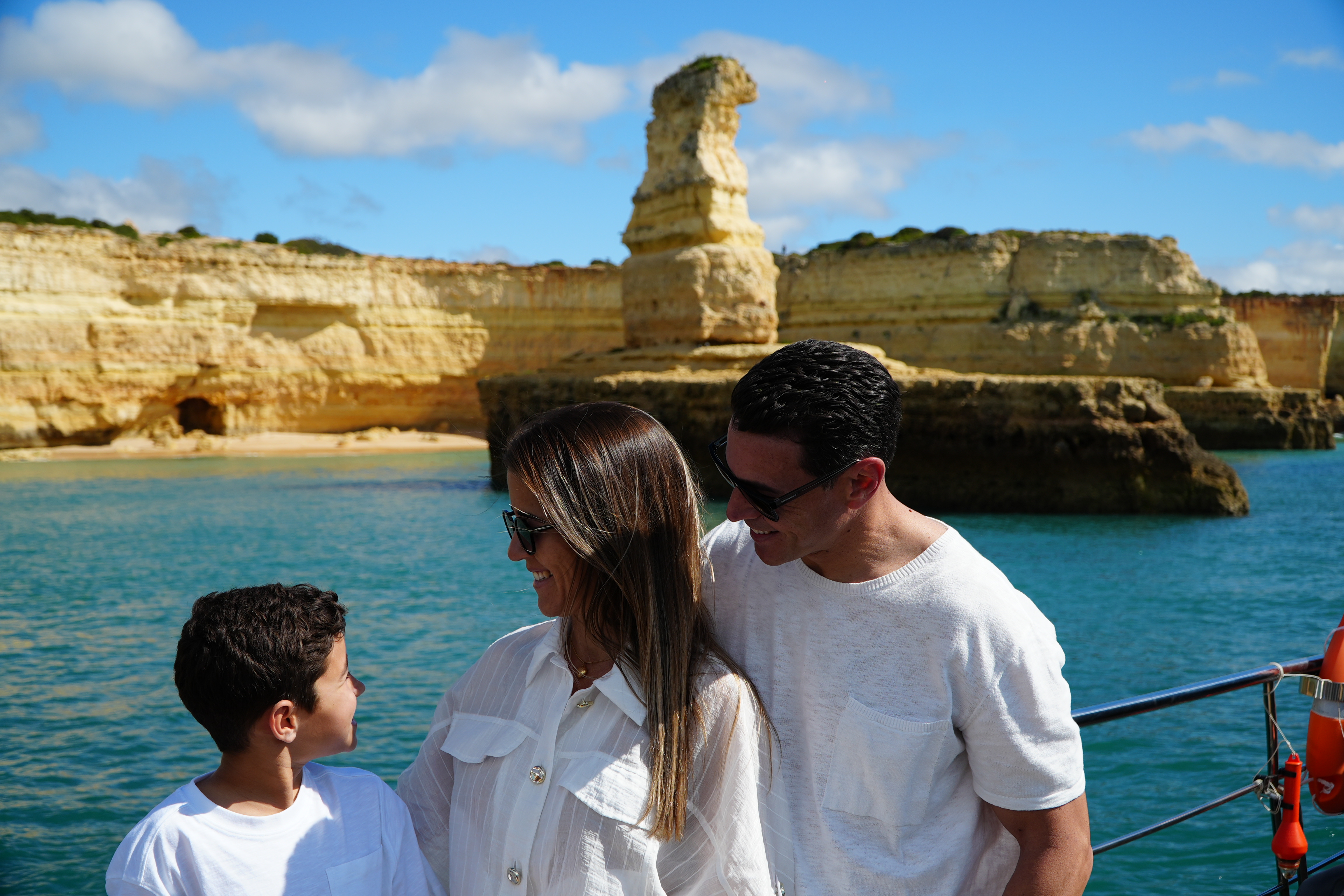 Une famille à bord d'un bateau profite de l'excursion en catamaran Portimão : Dauphins et grottes de Benagil proposée par AlgarExperience, avec les superbes falaises maritimes de l'Algarve en arrière-plan.