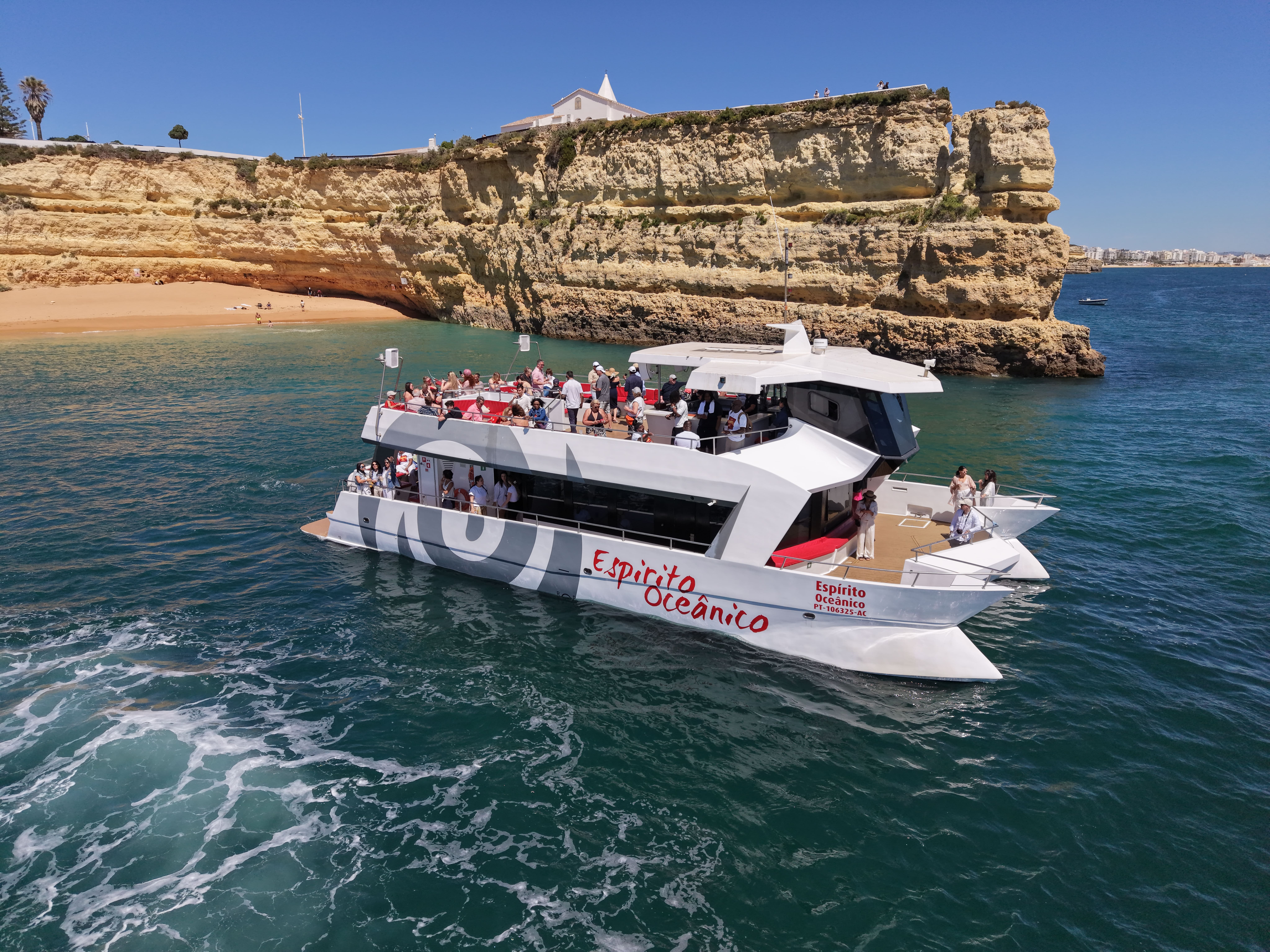 An AlgarExperience catamaran full of guests cruises along the golden cliffs of the Algarve during a Portimão: Benagil Caves Cruise with Brunch and Open Bar.