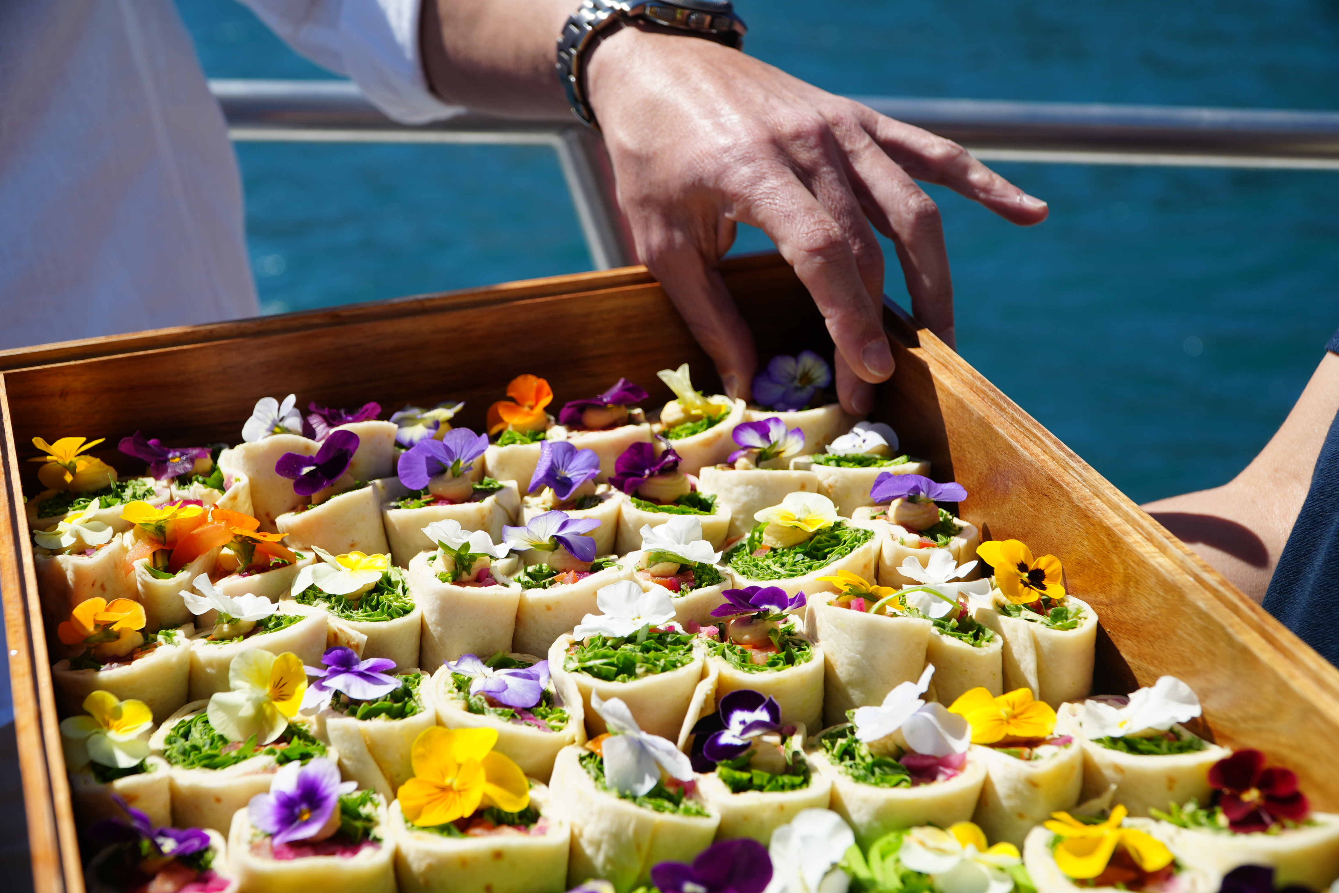 Un plateau en bois garni de wraps de brunch colorés, agrémentés de fleurs comestibles, est servi lors de la croisière Portimão : Benagil Caves Cruise with Brunch and Open Bar by AlgarExperience.
