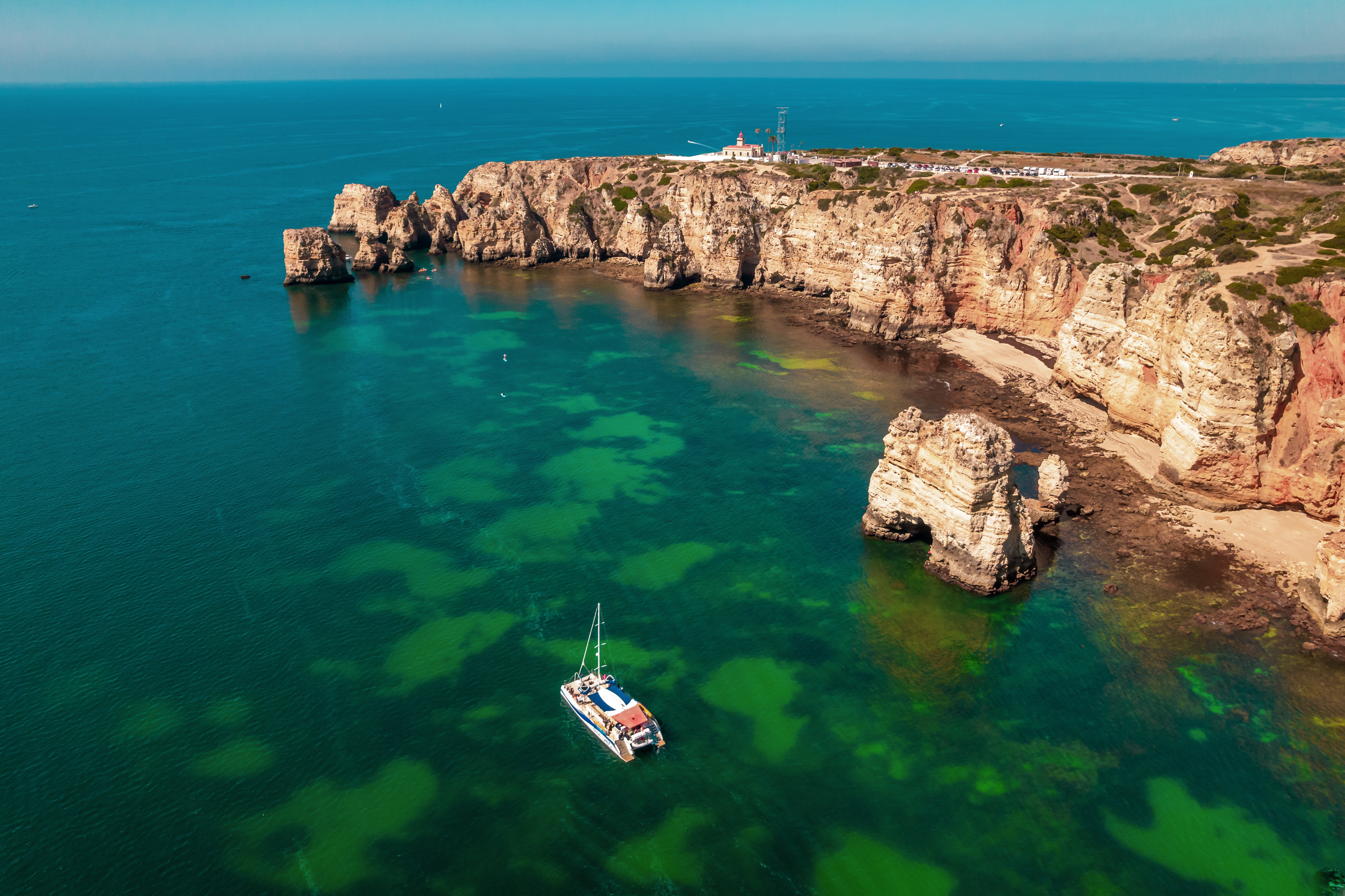 Ein AlgarExperience-Katamaran segelt auf dem türkisfarbenen Meer entlang der goldenen Klippen von Ponta da Piedade während der Katamarantour Lagos: Ponta da Piedade Caves.