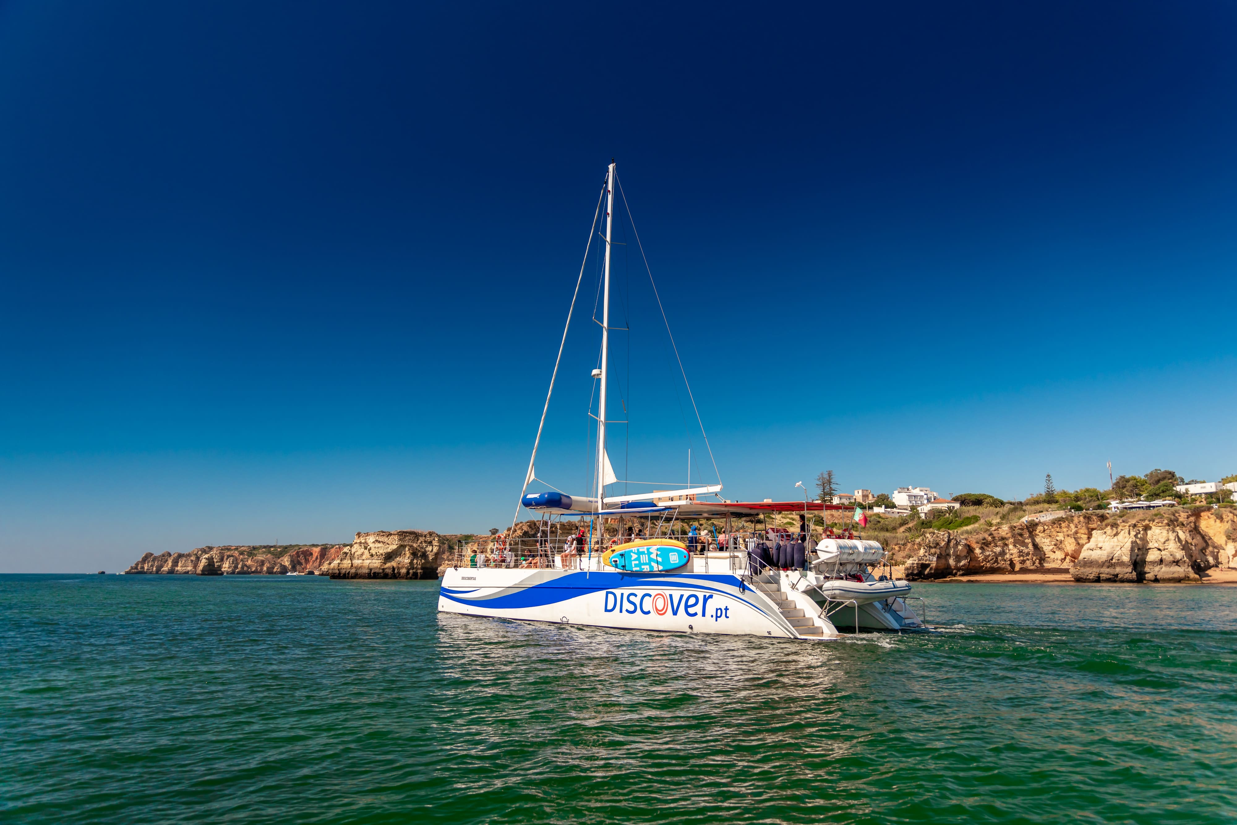 An AlgarExperience catamaran full of guests sails along the Ponta da Piedade coastline on a sunny day during the Lagos: Ponta da Piedade Caves Catamaran tour.