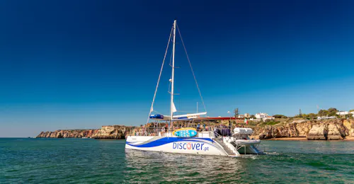 Catamarancruises langs de kustlijn van Ponta da Piedade Een AlgarExperience-catamaran vol gasten vaart op een zonnige dag langs de kustlijn van Ponta da Piedade tijdens de Lagos: Ponta da Piedade Caves Catamaran-tour.