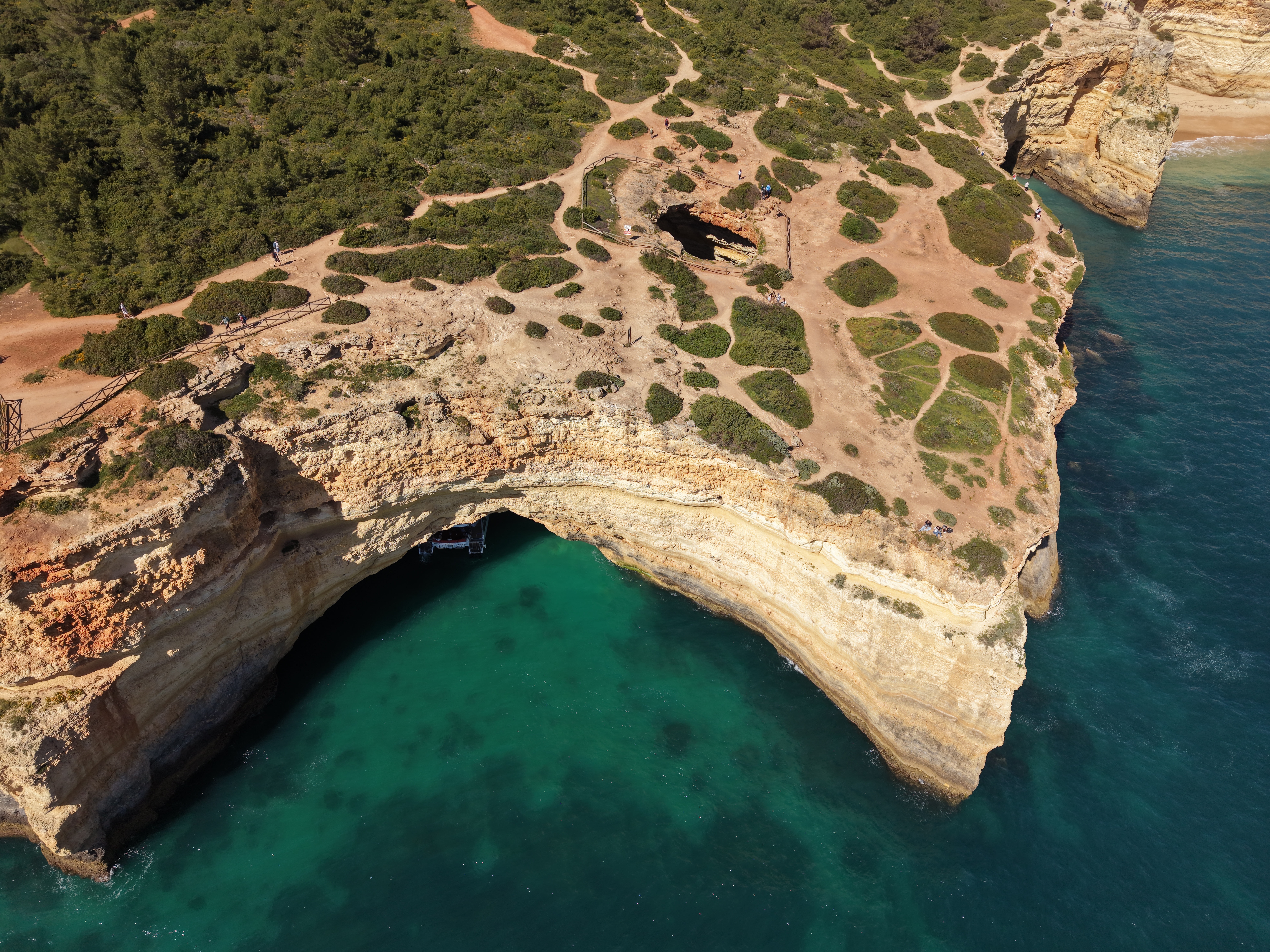 Luftaufnahme der atemberaubenden Benagil-Höhlen an der Küste von Portimão, wo ein Ausflugsboot von AlgarExperience vom türkisfarbenen Meer aus in die Grotte einfährt.