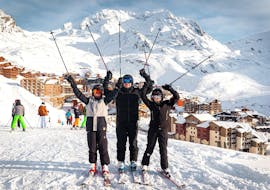 Due bambini e un istruttore della scuola di sci Ski Cool Val Thorens posano davanti alla stazione sciistica al termine delle lezioni private di sci per bambini e ragazzi.