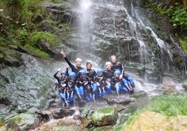 Two families with kids are posing for a picture under a waterfall during their Canyoning for Families in Zillertal with Freiluftakademie.
