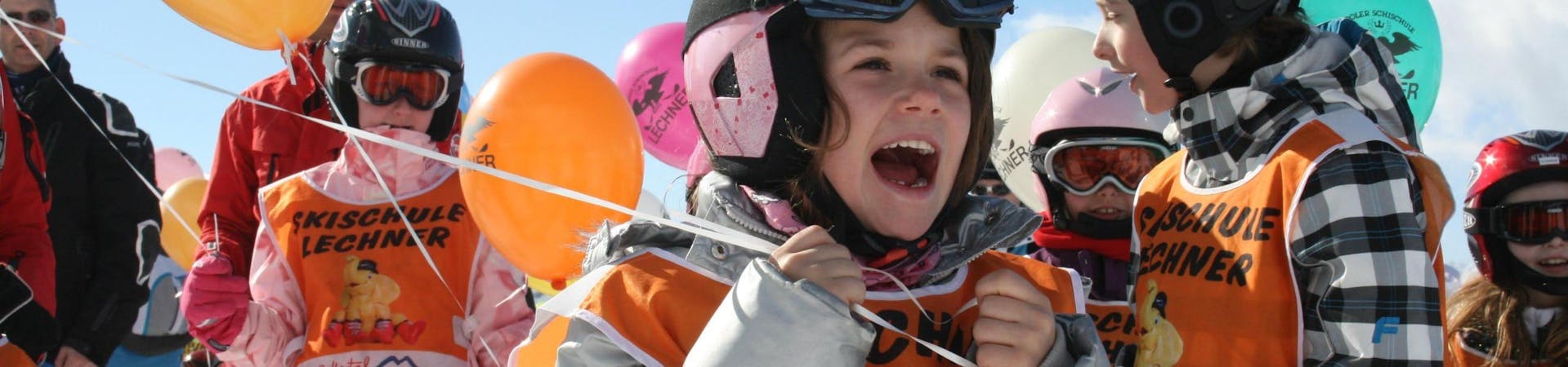 Verschillende kinderen die deelnemen aan de skilessen voor kinderen voor beginners (5-14 jaar), georganiseerd door de skischool Skischule Lechner, houden ballonnen vast met het logo van de skischool erop gedrukt.