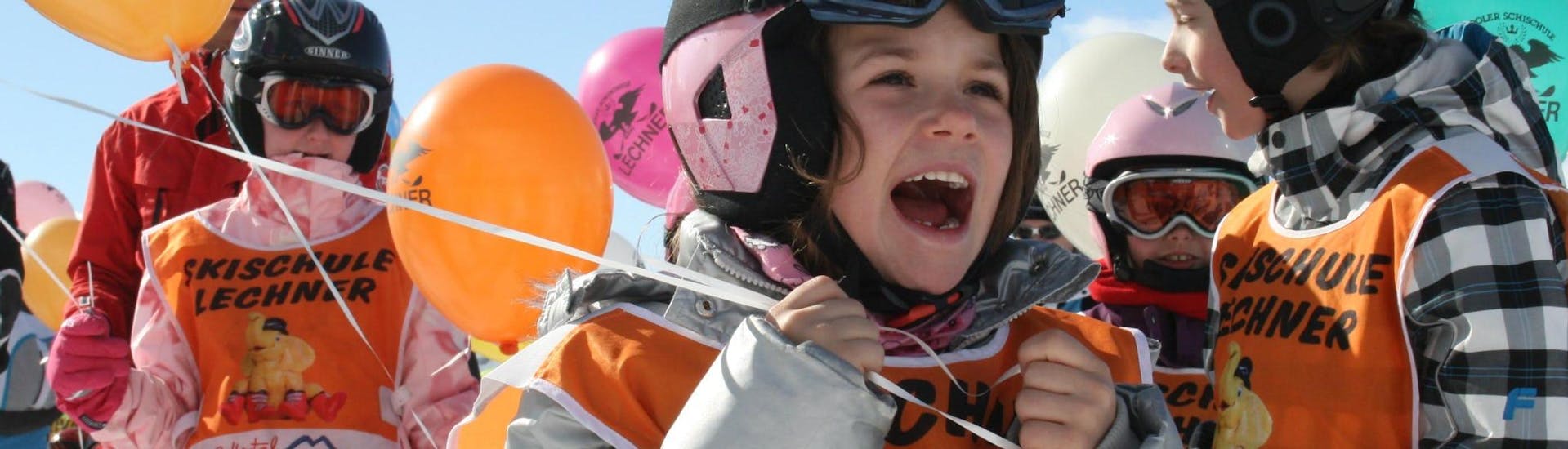 Verschillende kinderen die deelnemen aan de skilessen voor kinderen voor beginners (5-14 jaar), georganiseerd door de skischool Skischule Lechner, houden ballonnen vast met het logo van de skischool erop gedrukt.