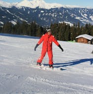 A snowboarding instructor from the ski school Skischule Lechner in Zell am Ziller is showing how to ride down the slope correctly during the Snowboarding Lessons for Adults - Beginners.