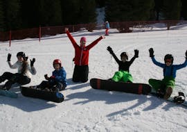 Een groep kinderen en hun snowboardleraar van de skischool Skischule Lechner in Zell am Ziller nemen een korte pauze in de sneeuw tijdens hun Snowboardlessen voor Kinderen (8-14 jaar) voor Beginners.