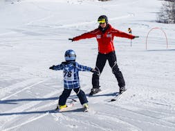 Een ski-instructeur van de Sport Aktiv Seefeld skischool skiet de piste achterstevoren en leert een peuter hoe je door de sneeuw moet ploegen in de "Mini" skilessen voor kinderen (3-5 jr.) voor beginners.