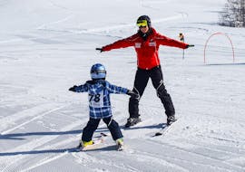 A ski instructor from the Sport Aktiv Seefeld ski school skis the slope backwards and teaches a toddler how to snowplough in the "Mini" kids ski lessons (3-5 yrs) for beginners.