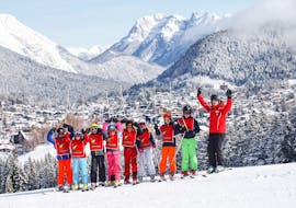 Eine Skigruppe mit ihrem Skilehrer bei ihrem Kinder-Skikurs "Maxi" (5-14 J.) für alle Levels in Seefeld stehen in einer Reihe und halten ihre Skistöcke nach oben.