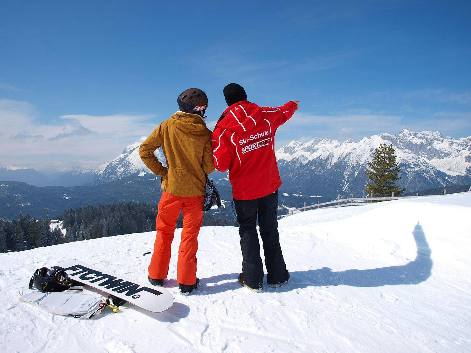 Cours particulier de snowboard pour Tous niveaux avec Ski School Sport Aktiv Seefeld Un moniteur de snowboard et un élève de l'école de ski Sport Aktiv Seefeld sont debout, dos à la caméra, et regardent le panorama de la montagne pendant leur Cours particulier de snowboard pour Tous niveaux.