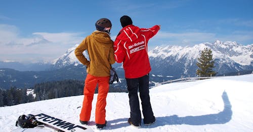 Private Snowboarding Lessons for Kids & Adults of All Levels from Ski School Sport Aktiv Seefeld A snowboard instructor and student from the Sport Aktiv Seefeld ski school stand with their backs to the camera looking out at the mountain panorama during their private snowboarding lessons for kids & adults of all levels.