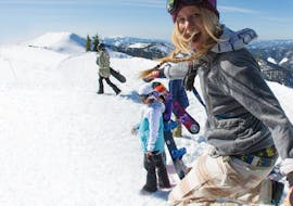 Eine glückliche Lehrerin zeigt ihren Schülern das Snowboarden beim Kinder-Snowboardkurs (bis 9 Jahre) der Snowboardschule Boardstars Schladming.